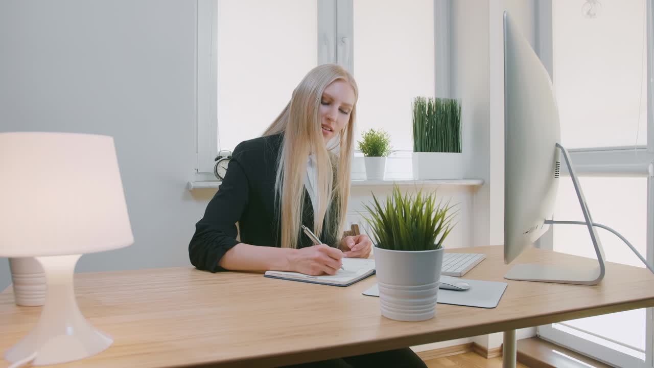 красивая деловая женщина, сосредоточенная на работе. привлекательная молодая блондинка в элегантной куртке, сидящая с ручкой и ноутбуком за столом с компьютером и взволнованно смотрящая на экран монитора.