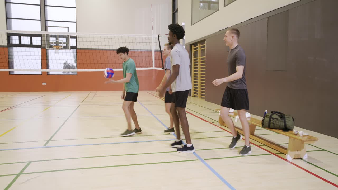 Colegas de equipe masculinos diversos colocando a bolsa de viagem no banco, pegando a bola de vôlei e indo para a rede para praticar passes.