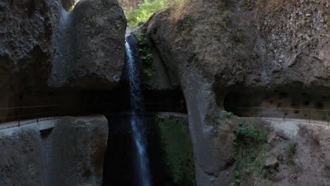 active woman runs behind famous levada do moinho waterfall in gorge, madeira