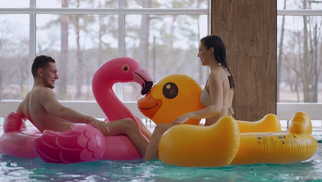 man and woman are having fun in pool riding funny inflatable swimming circle joyful couple