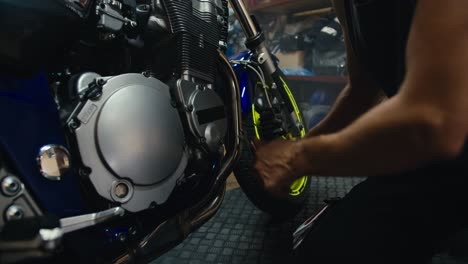 close-up shot of a male mechanic in a gray t-shirt using a tool to repair his blue motorcycle. a man with strong arms with visible veins works in a workshop