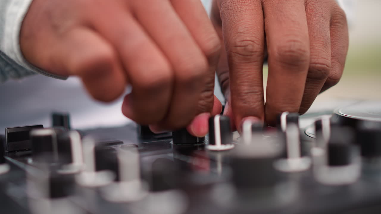 Primo piano delle mani del DJ sul mixer durante una sessione di pratica urbana all'aperto, dita che regolano manopole e fader con tecnica precisa, concentrazione tattile, luce naturale soffusa, attrezzatura dettagliata, musicista concentrato che modella il suono