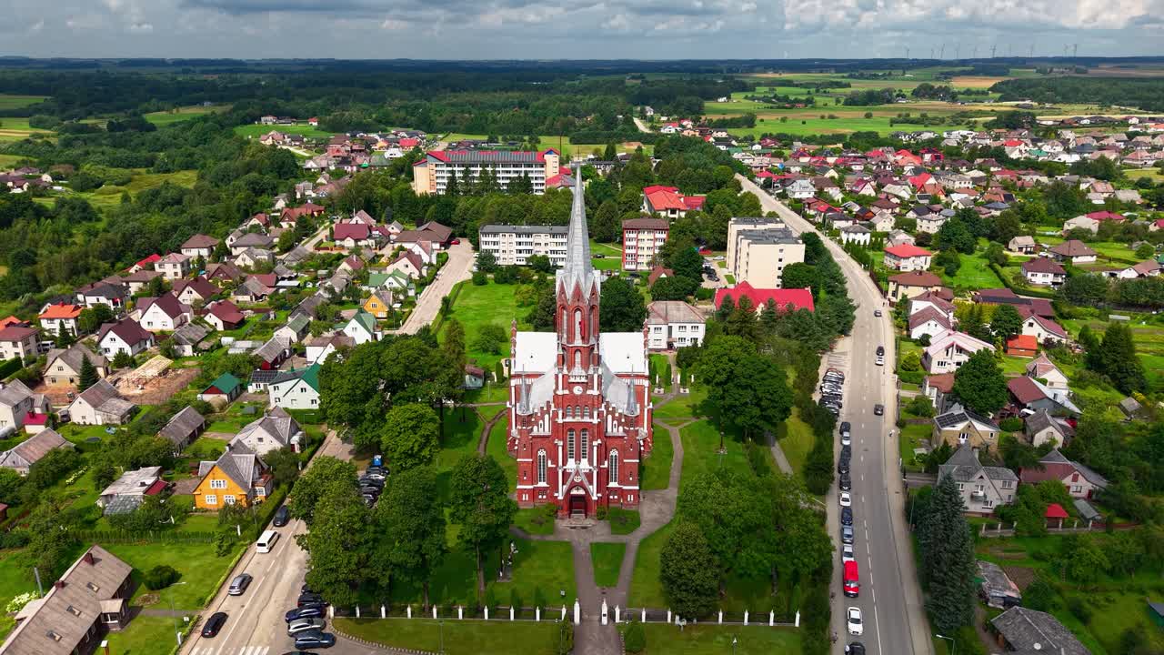 Aerial view of Šilalė St. Francis of Assisi Church surrounded by charming houses and green countryside in Lithuania. A peaceful small-town atmosphere with beautiful architecture