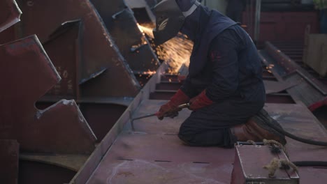 man working on a cargo ship is hammering a spot he just welded to make it's form good