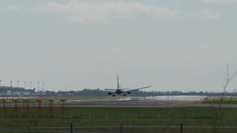 passenger aircraft approaching runway, descending over illuminated airport infrastructure and green landscape with security monitoring cameras against cloudy sky backdrop