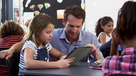 Teacher-and-young-schoolgirl-using-tablet-in-classroom