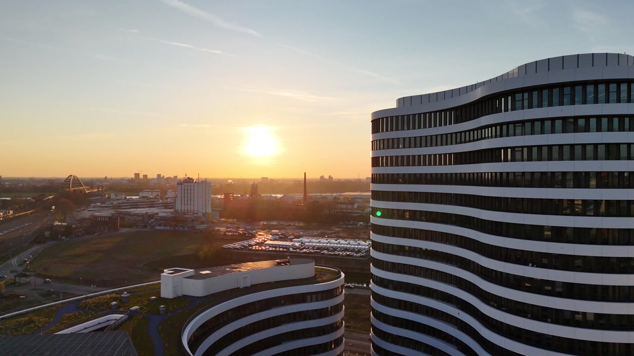 Drone flies straight toward layered white architecture in warm backlight with strong evening glow.