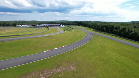 überflug von üppiger, grüner rennstrecke mit weichen flauschigen wolken und einem paddock voller exotischer autos