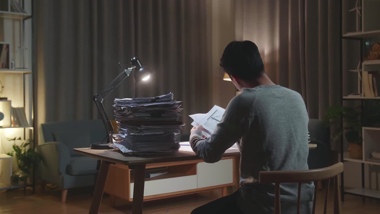Vista posteriore di un uomo asiatico stressato che getta via la carta mentre lavora con documenti a casa