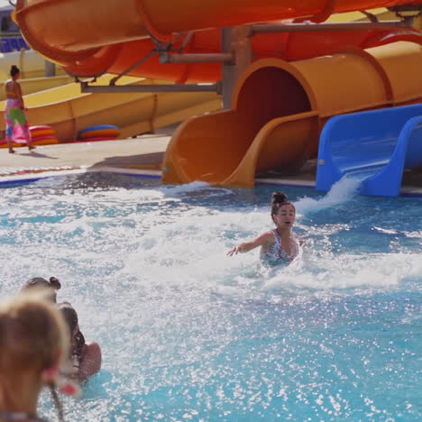 happy people in the water park. young woman sliding down into the blue water of the pool. beautiful water splashes outdoors. slow motion.