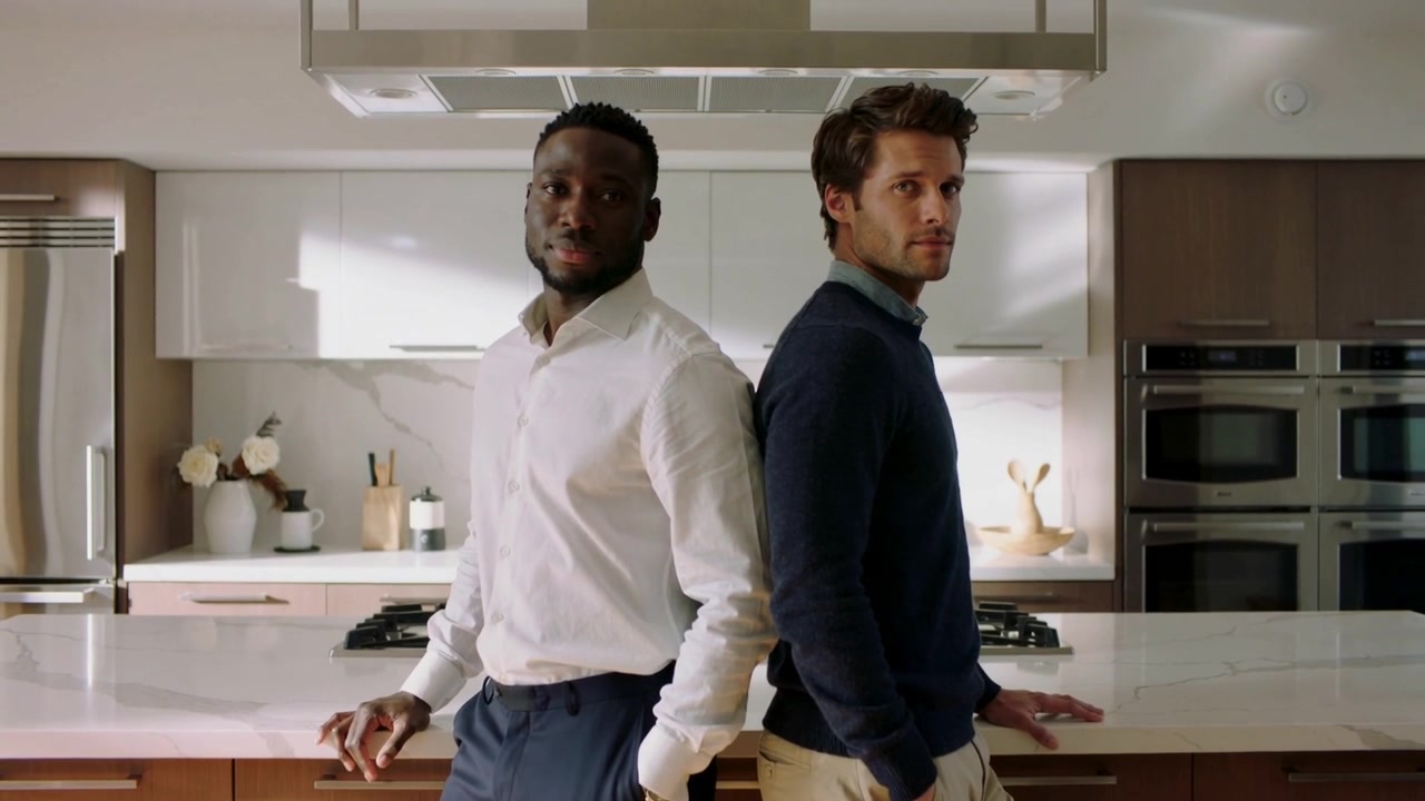 Camera filming two men in business wear posing back-to-back making minor moves in kitchen island