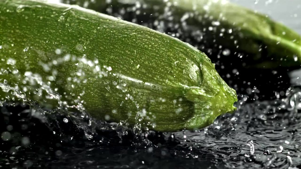 Zucchine verdi fresche con gocce d'acqua che schizzano al rallentatore.