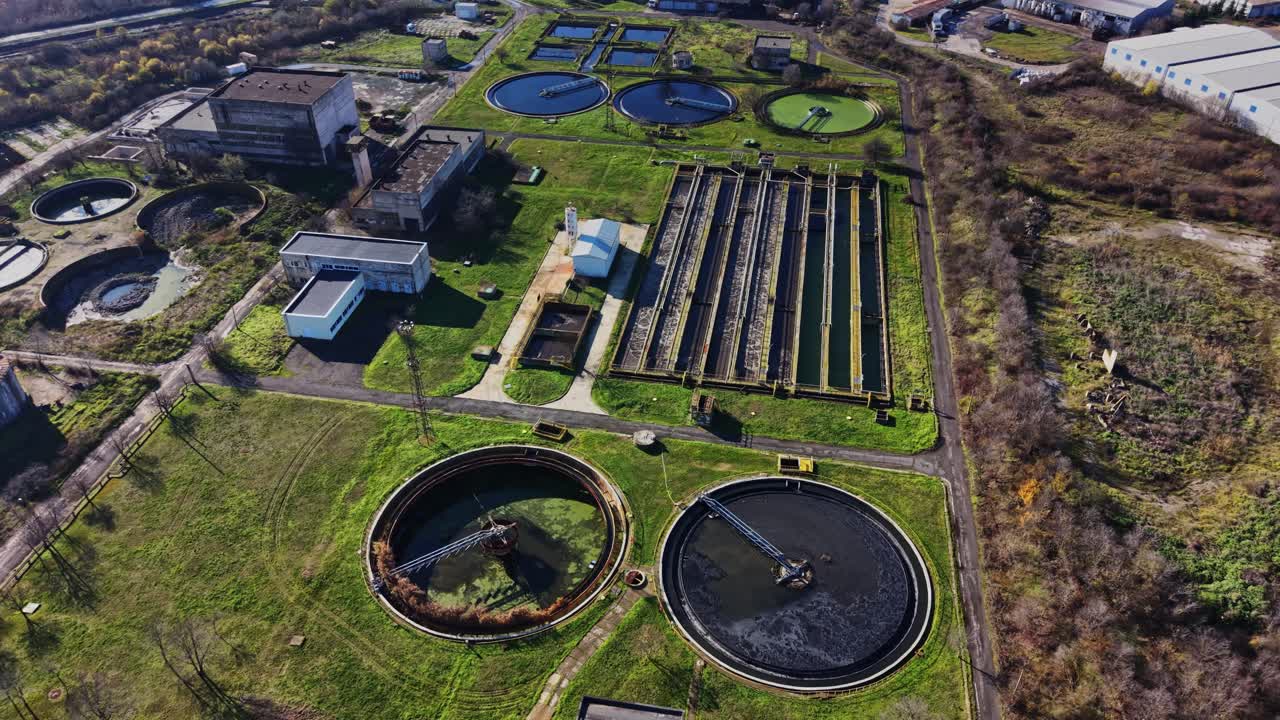 Water treatment facility with large tanks and greenery in daytime