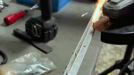 a close-up of a person using a powered metal saw to cut a screw, causing orange sparks to fly