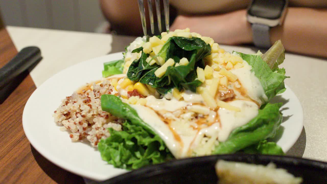 Close-up of woman dining on quinoa salad with fresh greens and creamy dressing, handheld shot