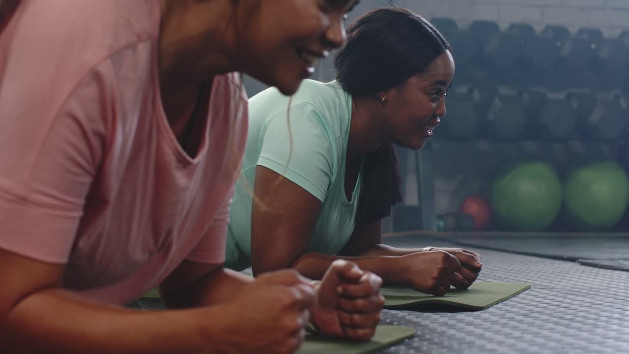 Diverse female friends holding forearm planks on mats at gym, camera panning, weights, toning core