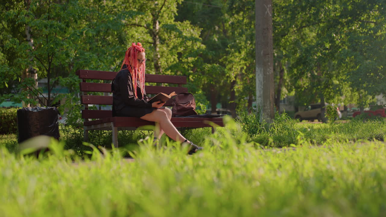 Женщина собирает сумку: кавказская дама с яркими косичками собирает чемодан в парке с наступлением вечера; женщина с ярко-розовыми волосами стильно укладывает свой багаж на скамейке во время теплого ночного отдыха в парке.