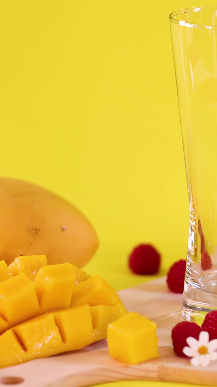 Cubetti di mango fresco, lamponi e ingredienti disposti per la preparazione di un frullato, con una luminosa illuminazione da studio.