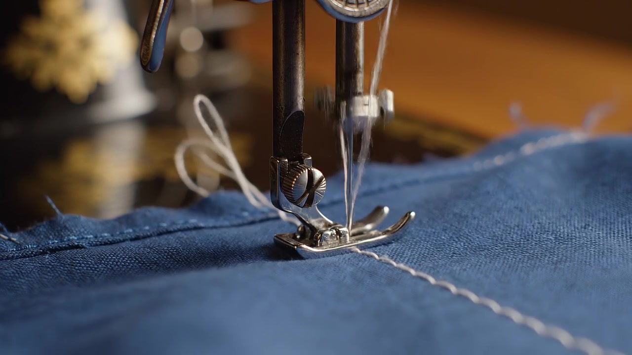 Close-up of vintage sewing machine foot stitching blue textile