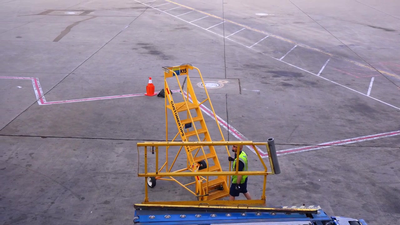 Chicago, USA, 7 May 2026: Ground perspective of an airport ladder stand, Chicago. Empty concrete tarmac with painted ground markings and a worker standing by the mobile stairs in bright sunlight.