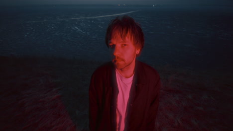 portrait of man standing near frozen lake under red light at night