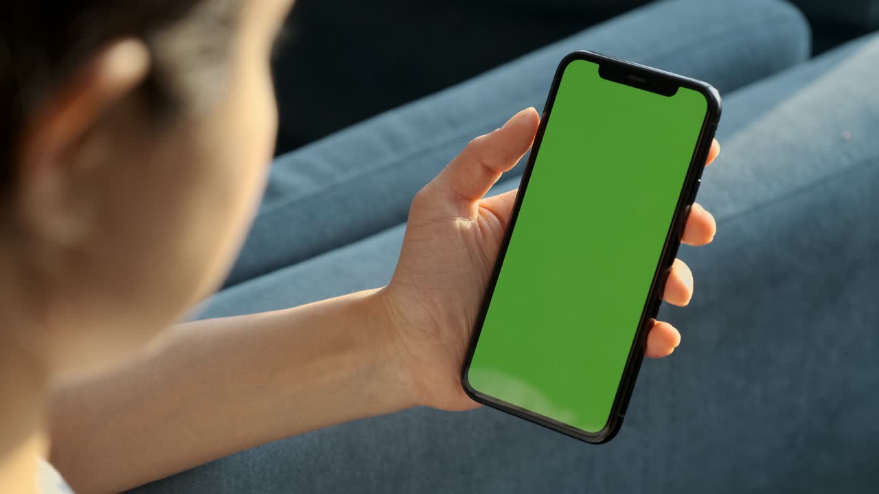 cámara portátil: vista trasera de una mujer morena sosteniendo una llave de croma pantalla verde teléfono inteligente viendo contenido sin tocar o deslizar. chica usando teléfono móvil, navegando por internet, viendo contenido
