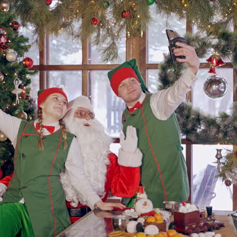 fairy elves photographing with santa claus. santa with white beard and elves in green costumes doing selfies on christmas holidays. christmas decorations.
