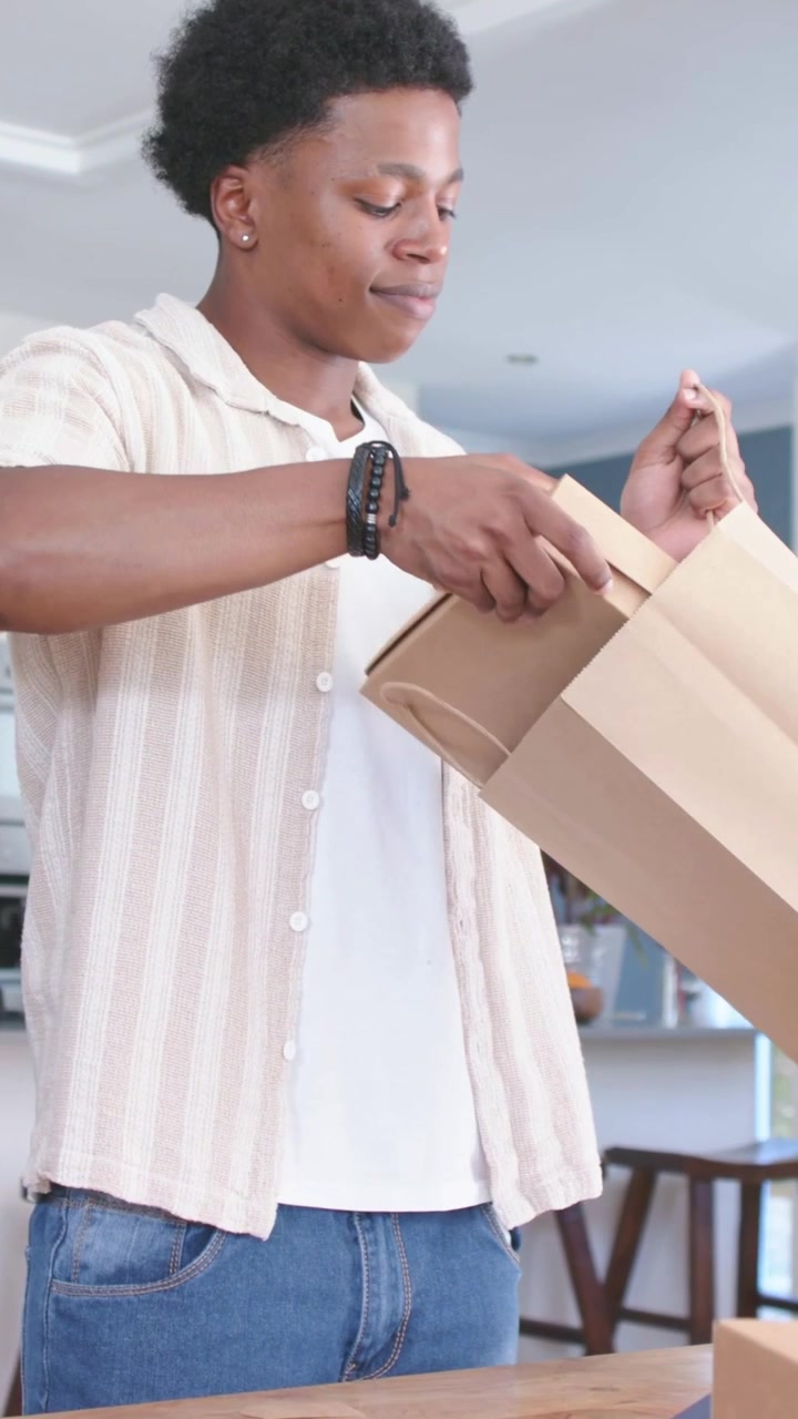 Adult man grasping bag handles, lifting flat boxes, inspecting, placing aside while unpacking items