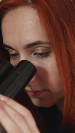 female student examines new type of bacteria through microscope on blurred background. woman with ginger hair does research in laboratory closeup