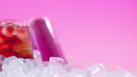 close up of chilled cold drink in glass poured from can on ice cubes against pink background 2