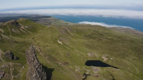 Aerial-view-revealing-Old-Man-Storr-in-Scotland's-lush-countryside-with-the-North-Sea-off-in-the-distance