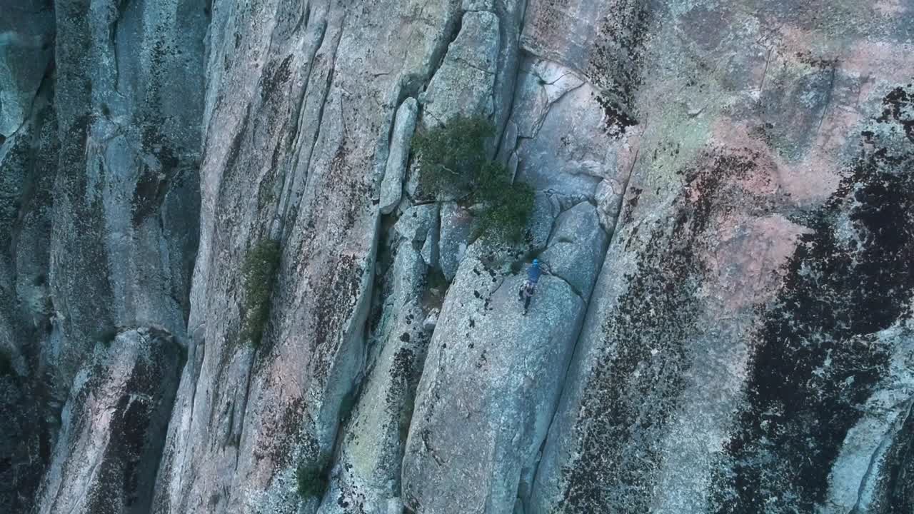Ascending aerial drone shot focused on a tiny climber while ascends by a granite rock wall