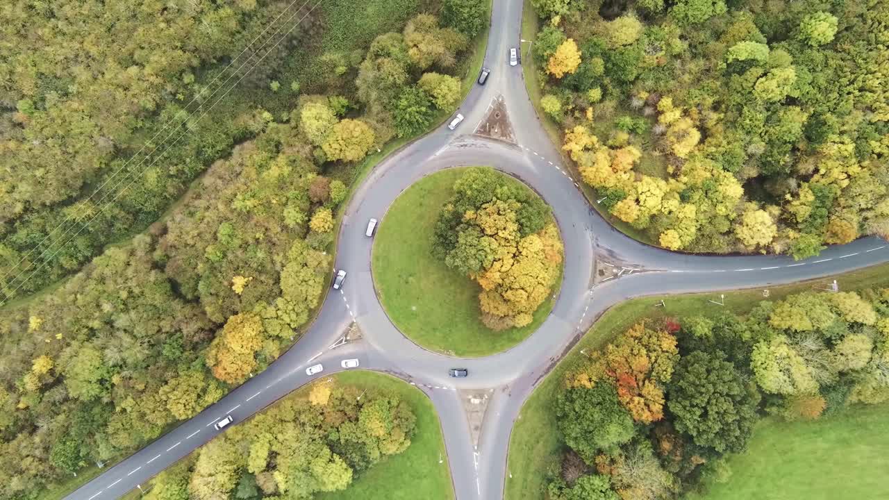 Aerial descending top view over roundabout traffic vehicles urban grassy countryside