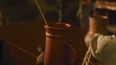 attendant puts dry straw into knight drink in tavern. caring innkeeper treats alcohol beverage for noble lord in armour at counter closeup. medieval inn