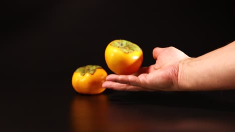 a hand skillfully balances persimmons on a table