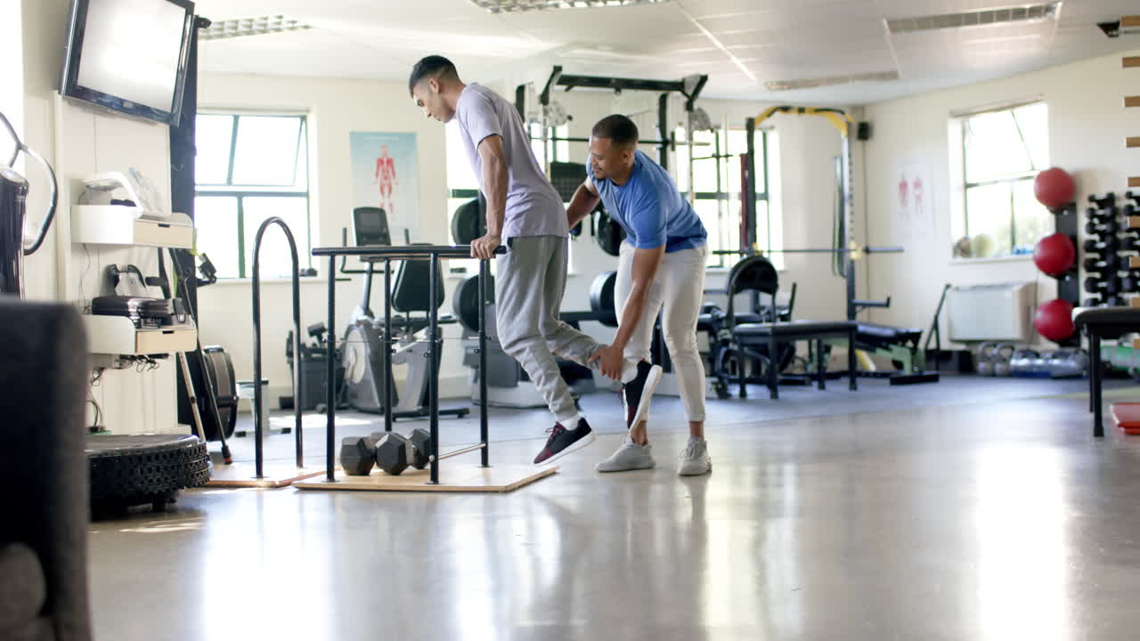Assisting man with disability, trainer supporting during parallel bars exercise