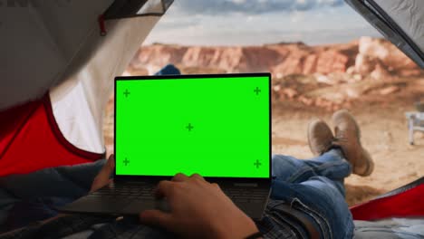 pov imágenes de un turista usando una computadora portátil con un marcador de lugar de pantalla verde en exhibición. viajero descansando en una tienda en la cima de una montaña rocosa. excursionista aventurero que vive en la naturaleza en el aire libre.