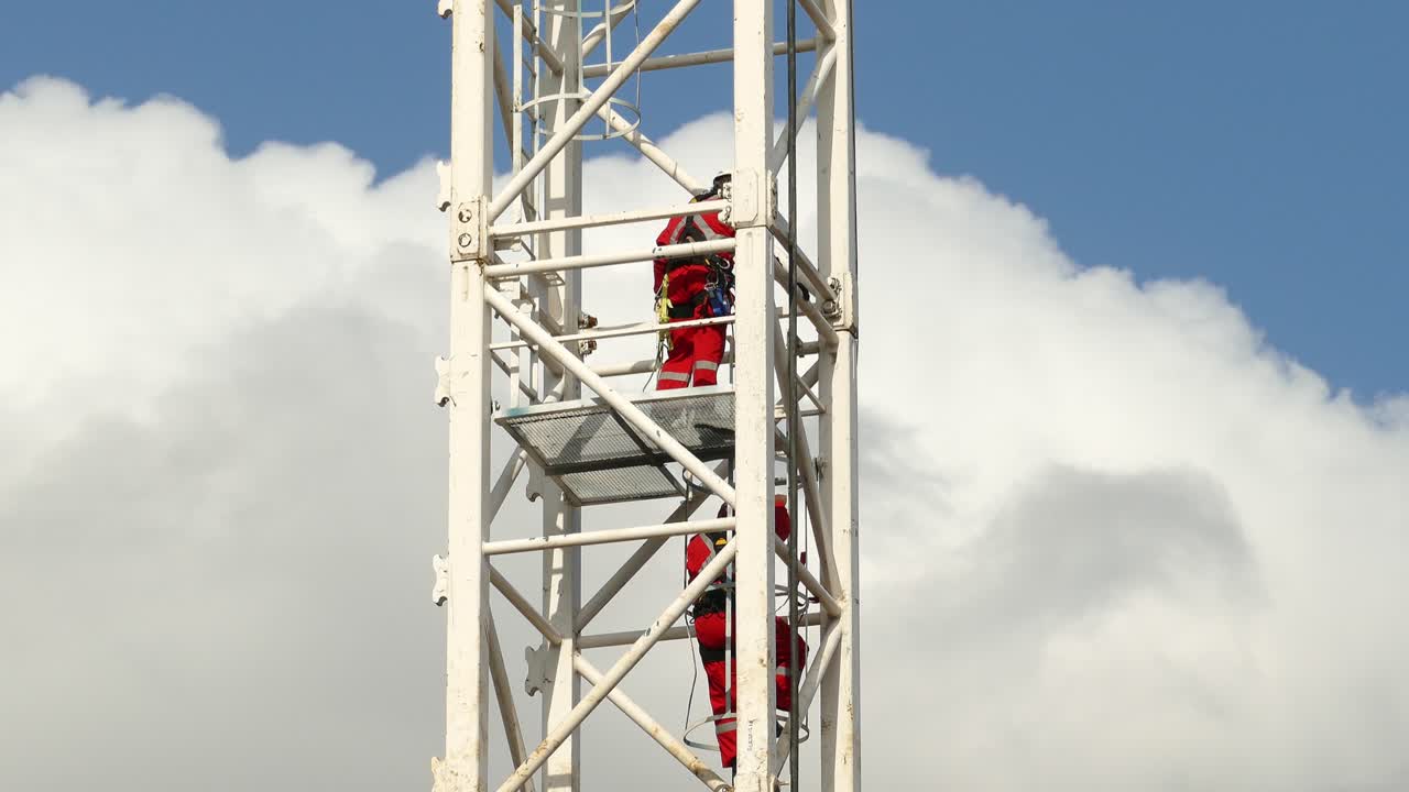 두 명의 구조 소방관이 높은 금속 전기탑에서 내려오고 있습니다.