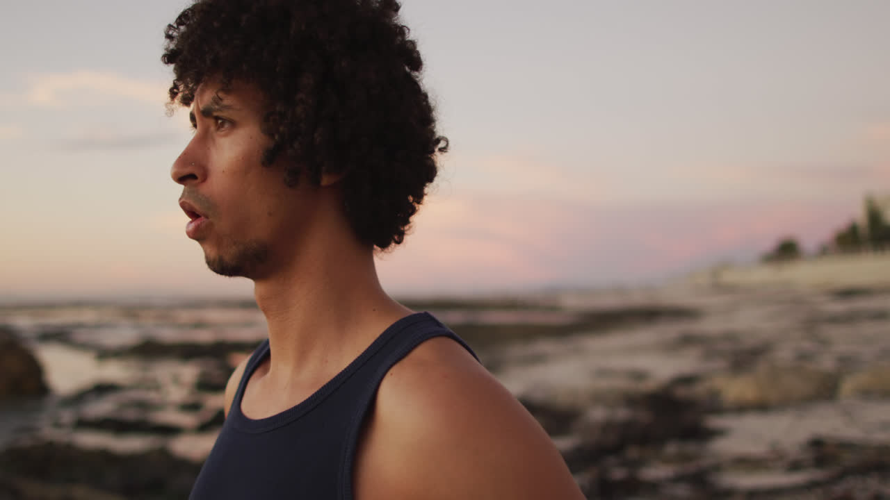 Tired african american man standing on the rocks near the sea during sunset