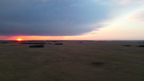 orange, vibrant sun setting in between a heavy cloud blanket and a flat, vast countryside landscape