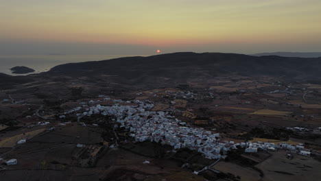 panoramic drone footage of kythnos chora at sunset, with golden light washing over white cycladic homes beneath a clear summer sky