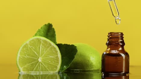 dripping oil from pipette into bottle close-up, lime juice. making aroma serum on yellow background. dropping liquid citrus extract, skincare routine, treatment spa concept. traditional medicine