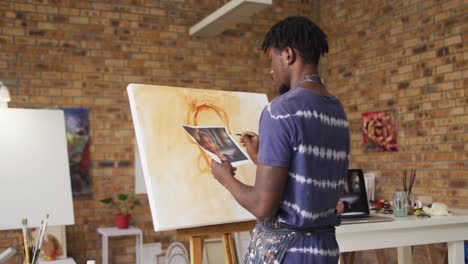 pintor afroamericano de sexo masculino pintando a partir de una fotografía en lienzo en el estudio del artista