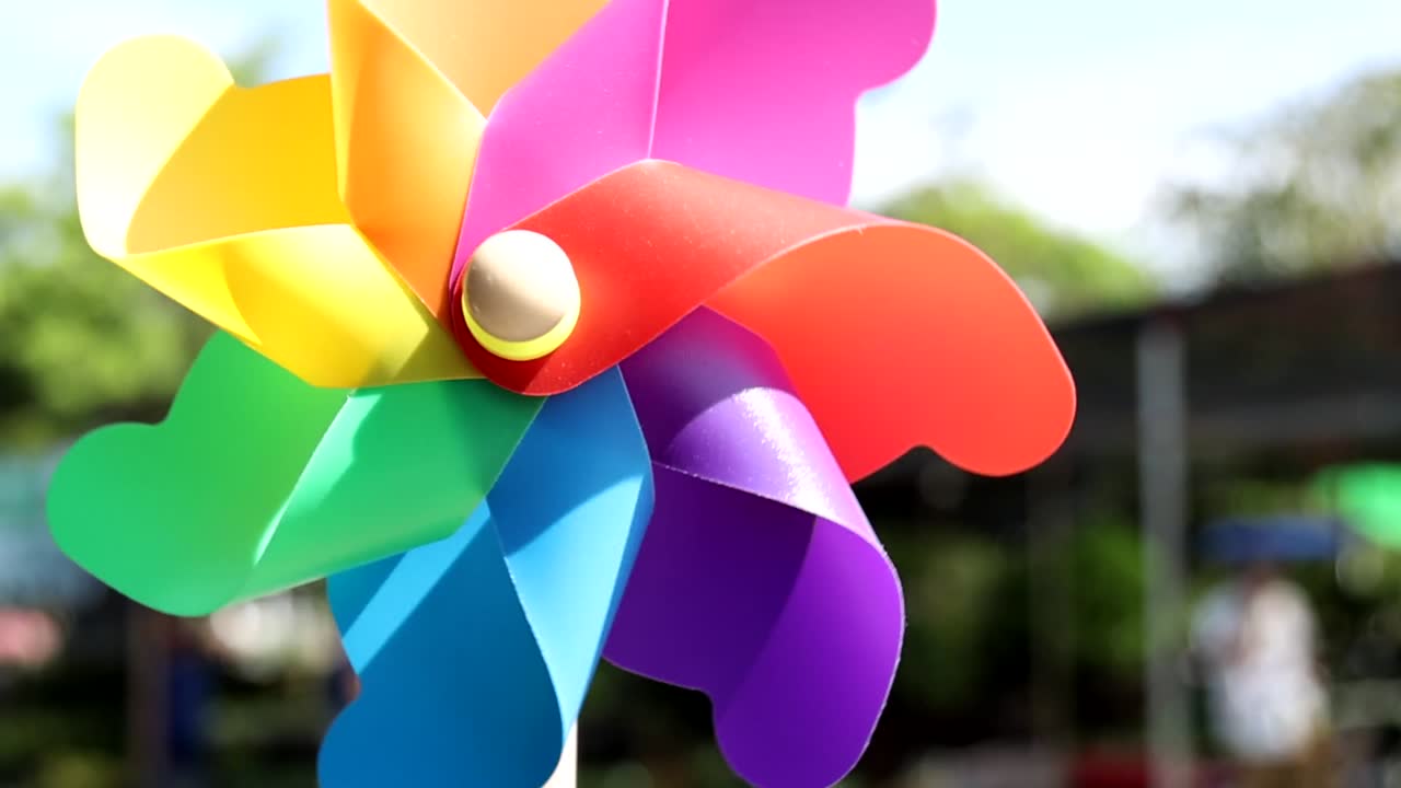 A colorful pinwheel spins energetically against a sunny garden backdrop, showcasing its vivid hues and dynamic motion.