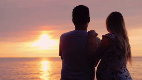 asian man with pregnant wife enjoy sunset over the ocean