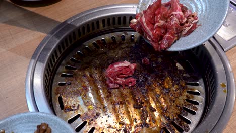 chef usando palillos para poner carne cruda en una sartén caliente, vista de cerca