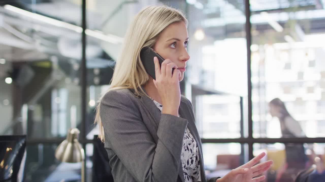 Imprenditrice caucasica che parla allo smartphone con colleghi che lavorano sullo sfondo