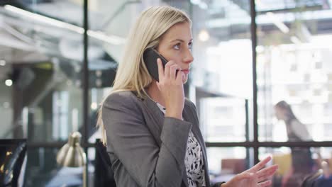 Caucasian-businesswoman-talking-on-smartphone-with-colleagues-working-in-background