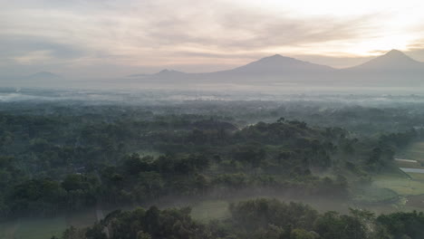 Silhouetted-Borobudur-temple-in-mystic-Indonesia-landscape,-dramatic-sunbeams-dancing-in-early-morning-mist