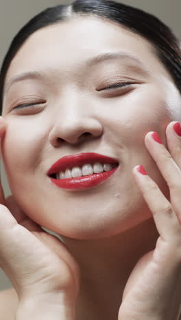 vertical video of asian woman with black hair and make up touching face, copy space, slow motion